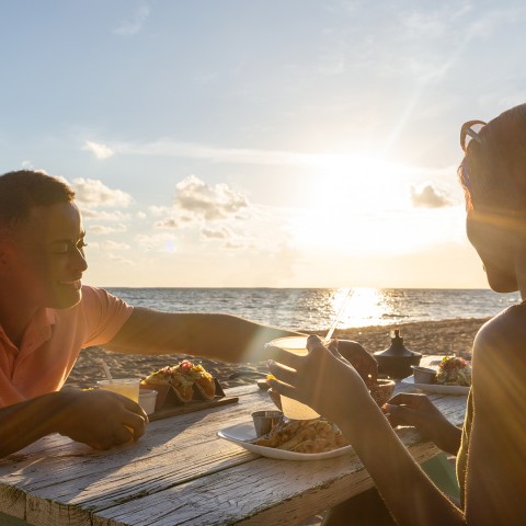 a couple of people sitting at a table with food on the beach