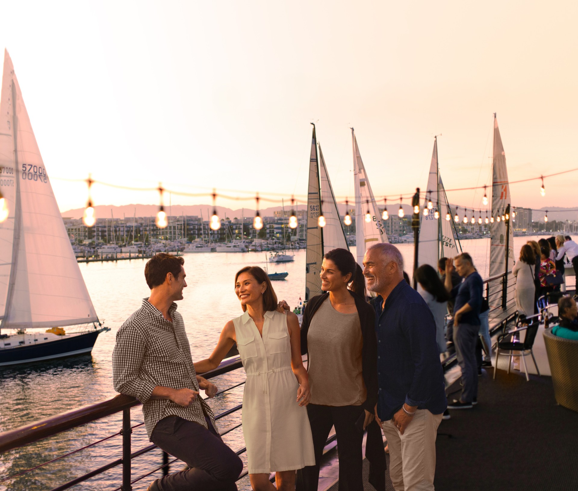 a group of people standing on a deck with sailboats in the background