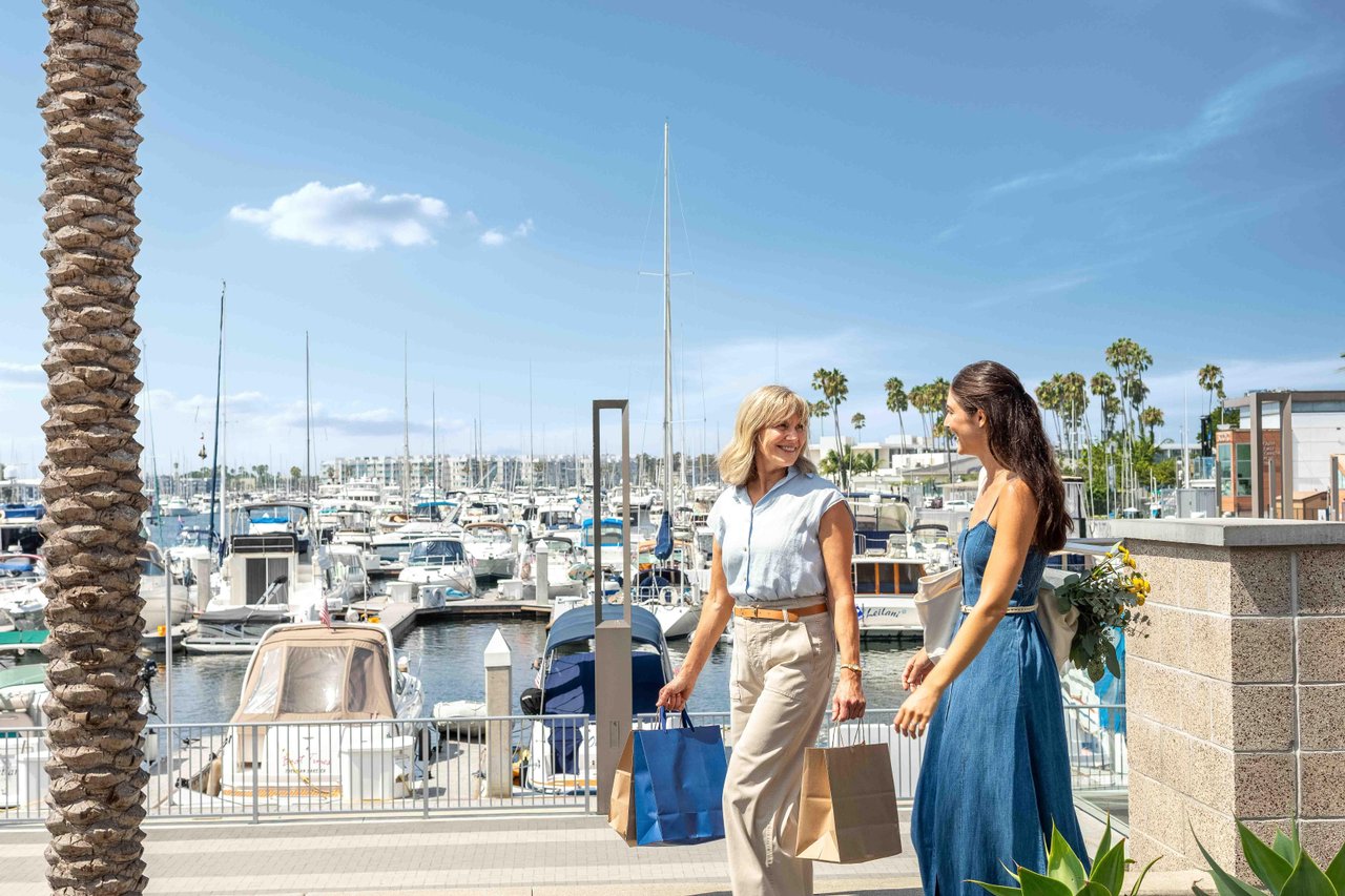 a couple of women walking on a dock with boats in the background