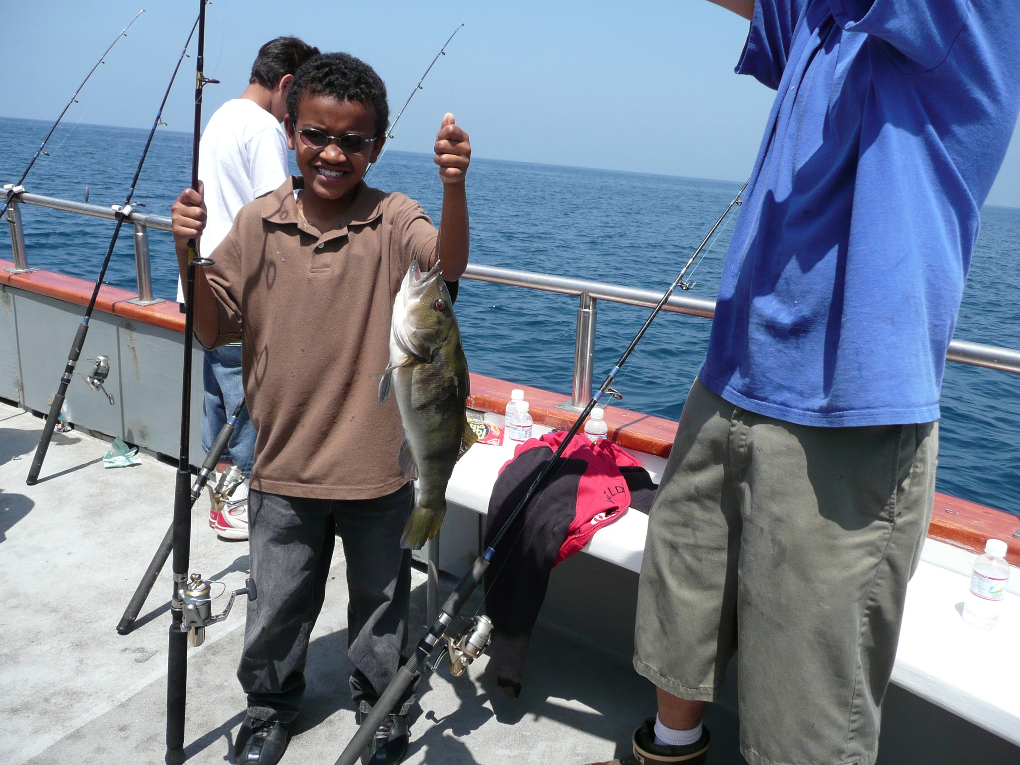 a boy holding a fish and standing next to a man on a boat