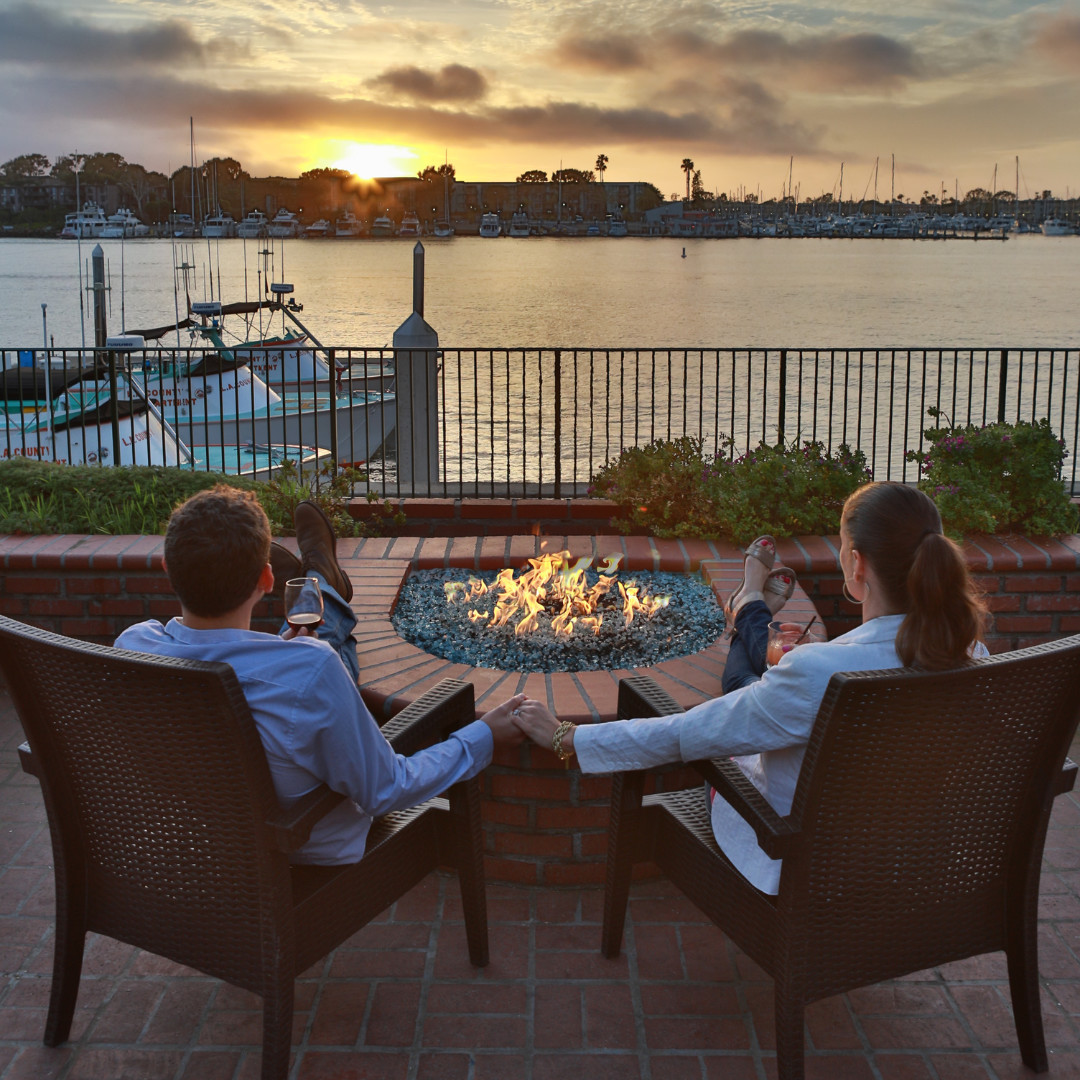 a couple sitting in chairs by a fire pit with a body of water in the background