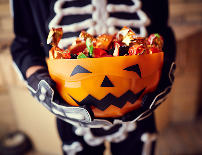 a person in a skeleton garment holding a bowl of candy