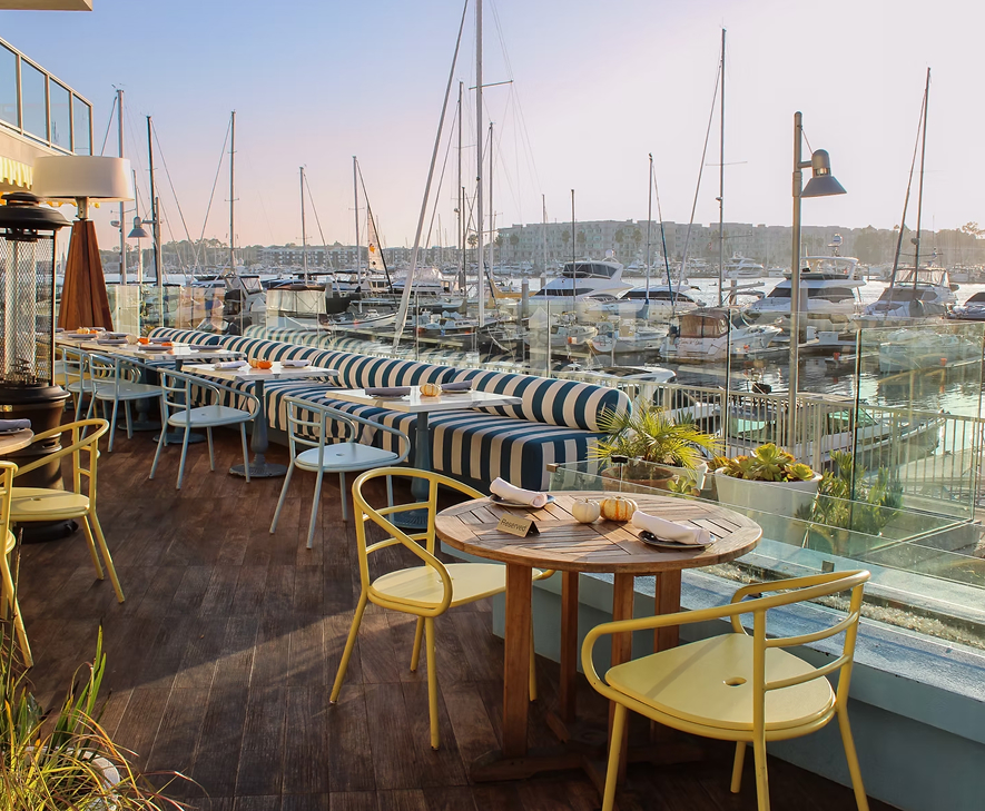 a table and chairs on a deck with boats in the background