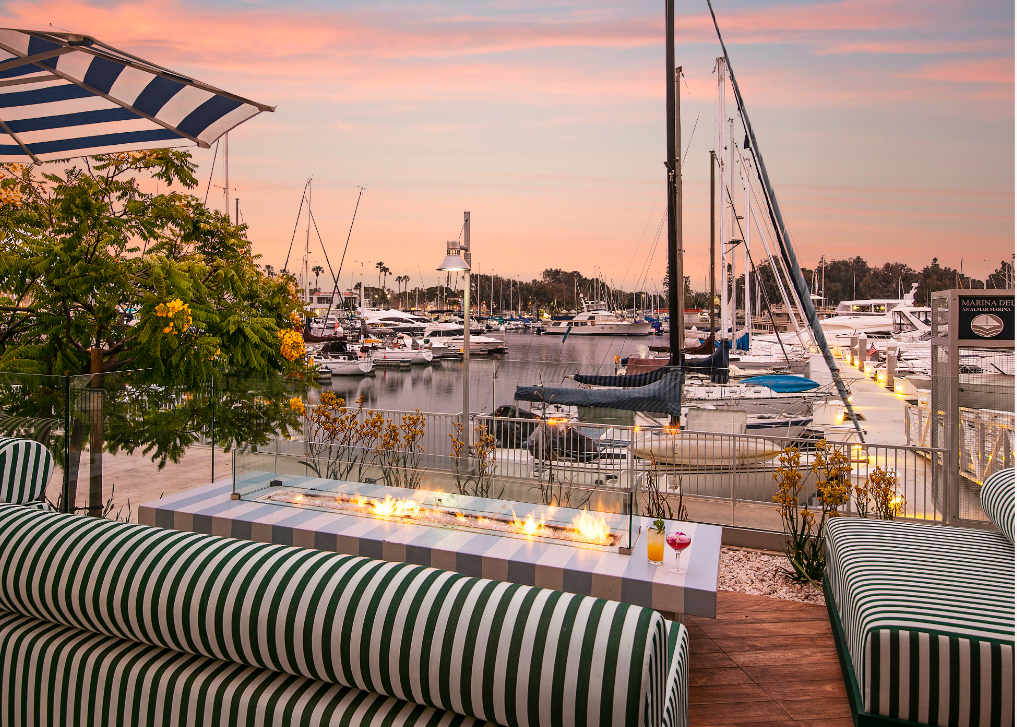 a table with a glass table and chairs with a view of a marina and boats and a sunset