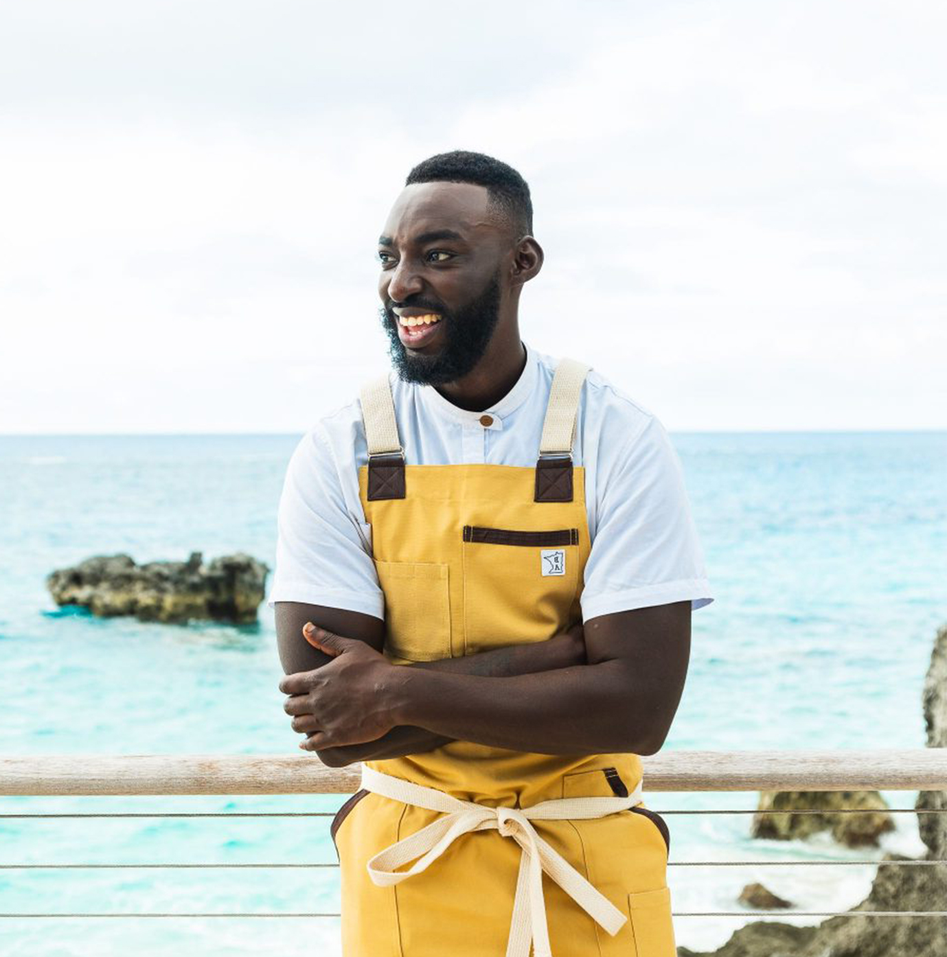 a man wearing yellow overalls standing by a railing with water in the background