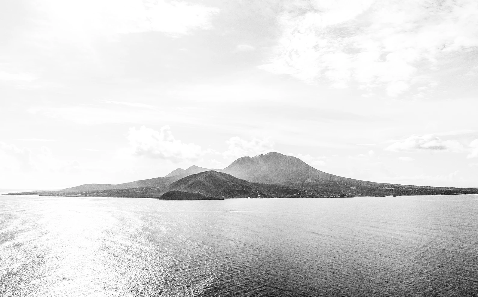 a black and white photo of a body of water with a mountain in the distance