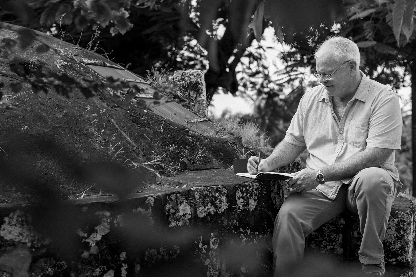 a man sitting on a ledge writing on a book
