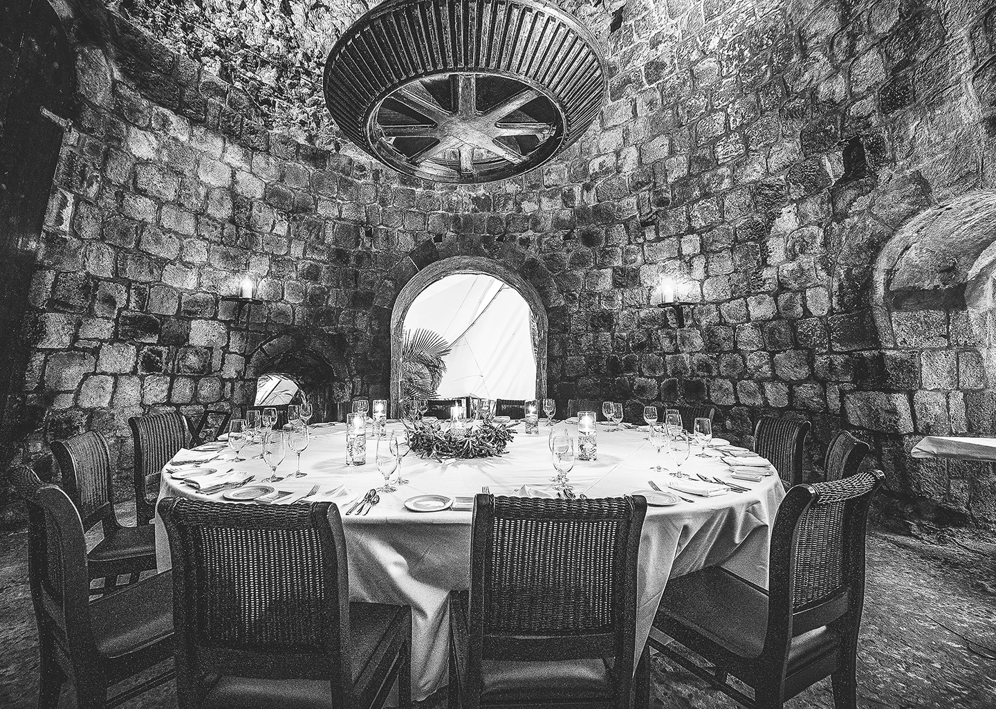 a round table with a white tablecloth and chairs in a stone room