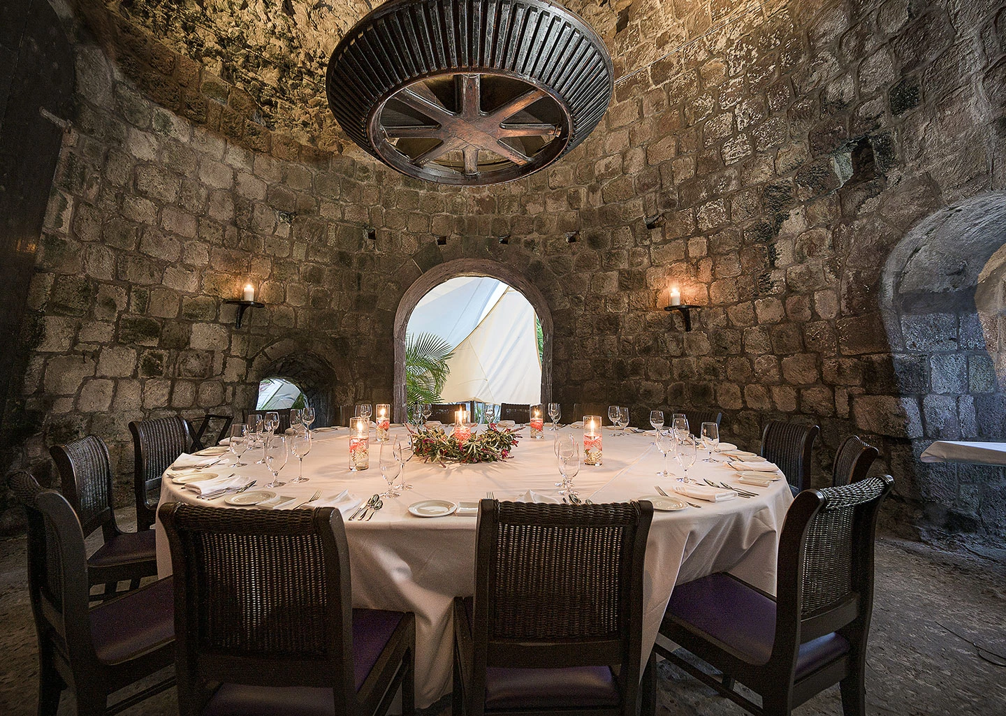 a round table with candles and chairs in a stone room