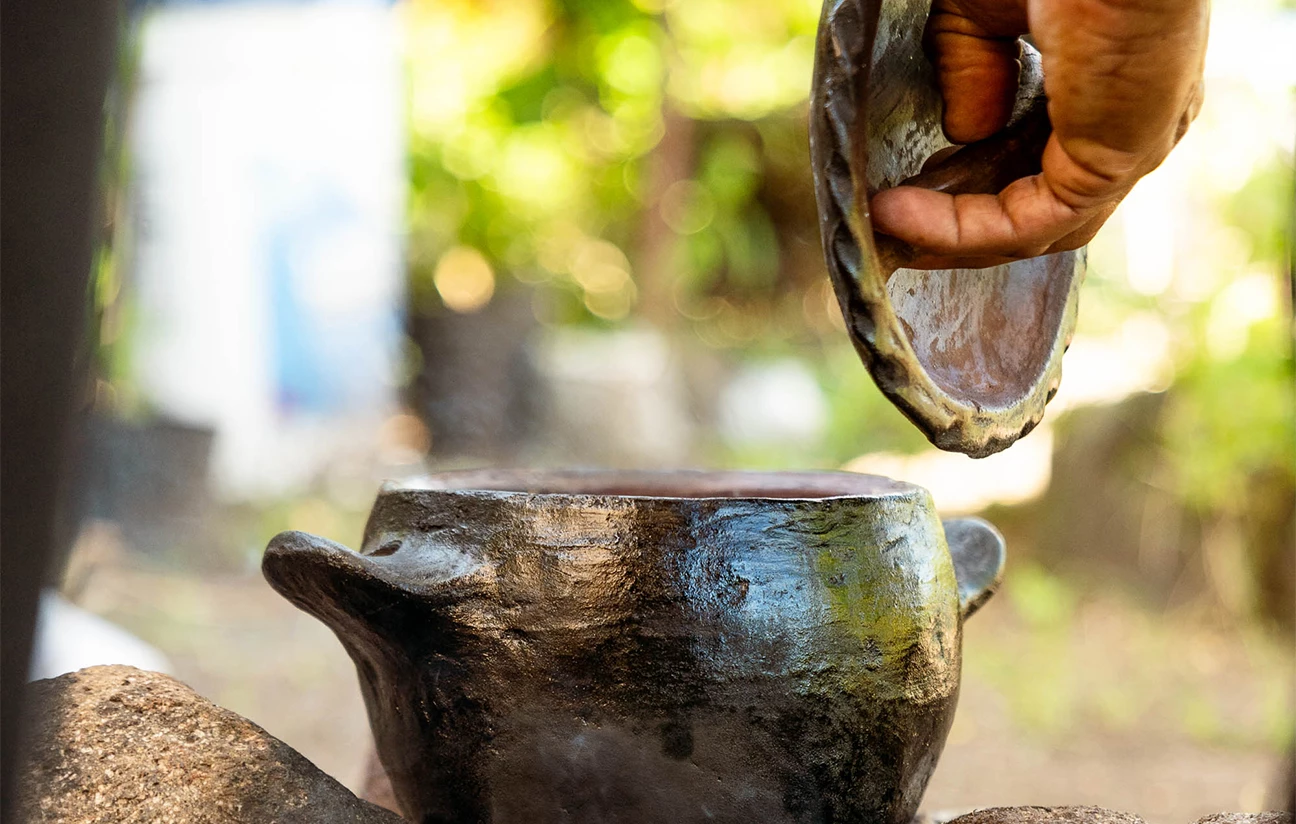 a hand pouring a clay pot into a pot