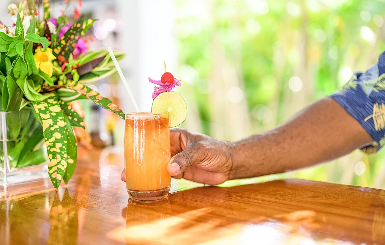a hand holding a glass of orange liquid with lime slices and a straw