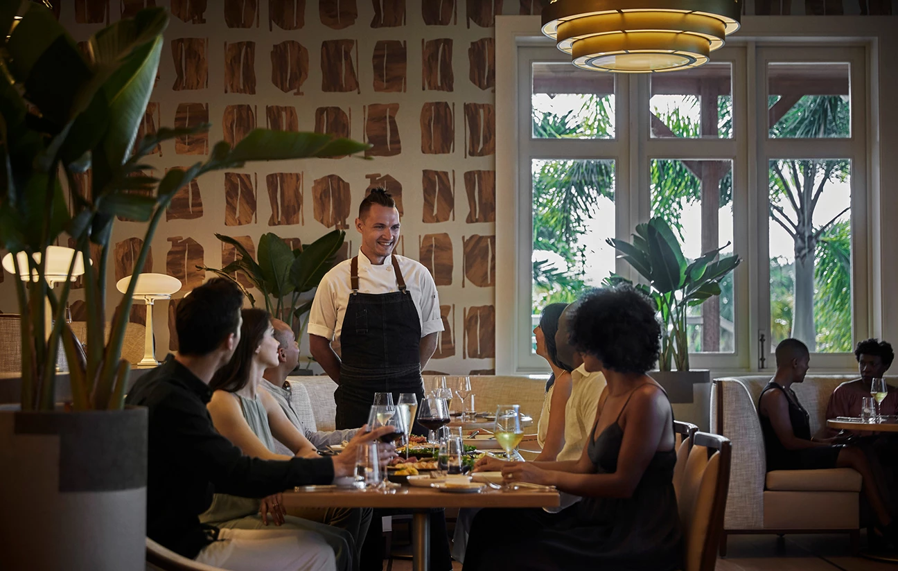 a man standing in front of a group of people sitting around a table
