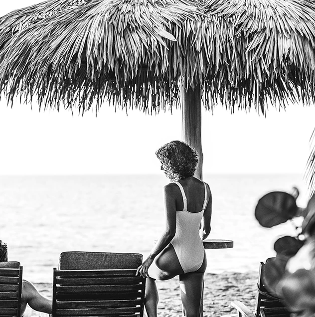a woman in a bathing suit under a straw umbrella on a beach