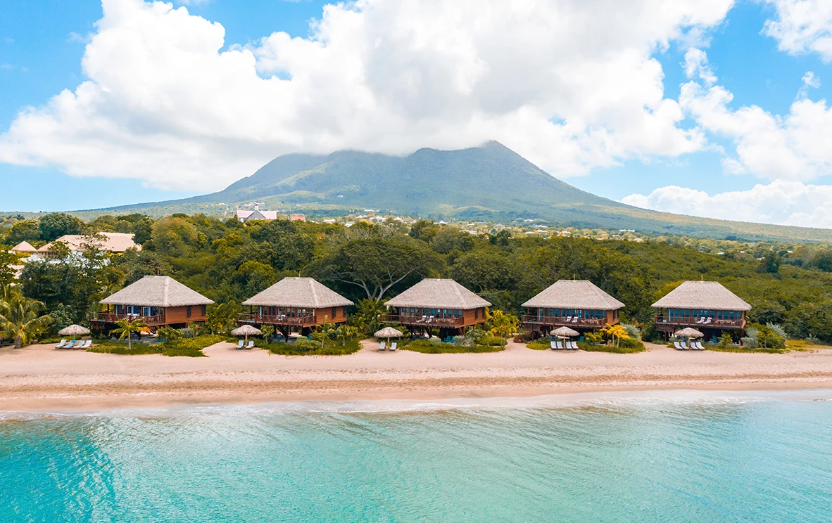 a group of huts on a beach with Nevis in the background