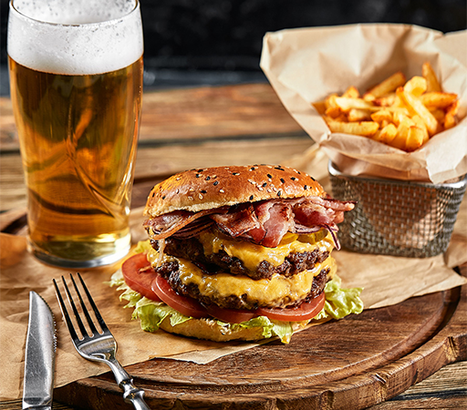 a double cheeseburger with bacon and fries on a wooden board