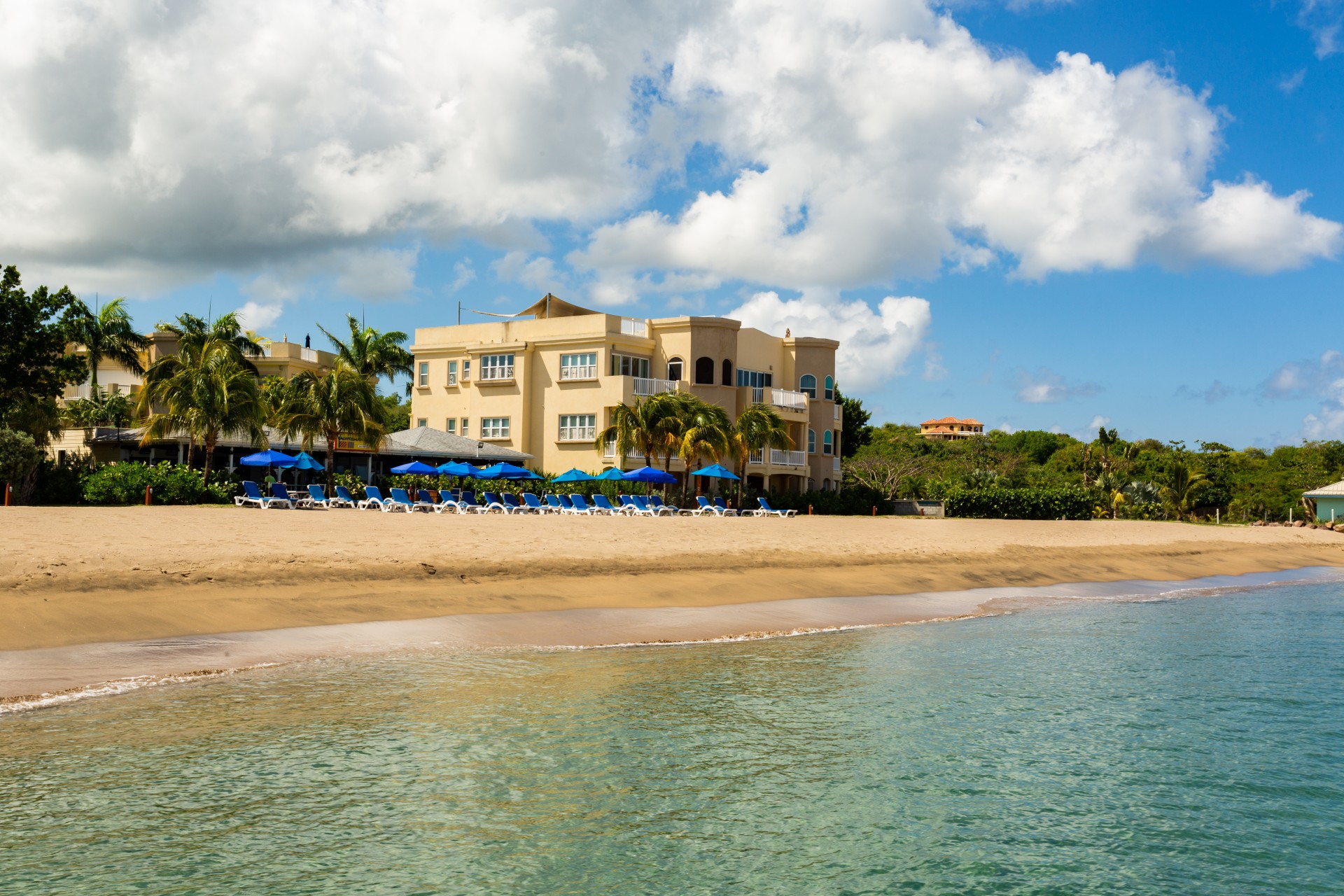 a beach with a building and chairs and umbrellas