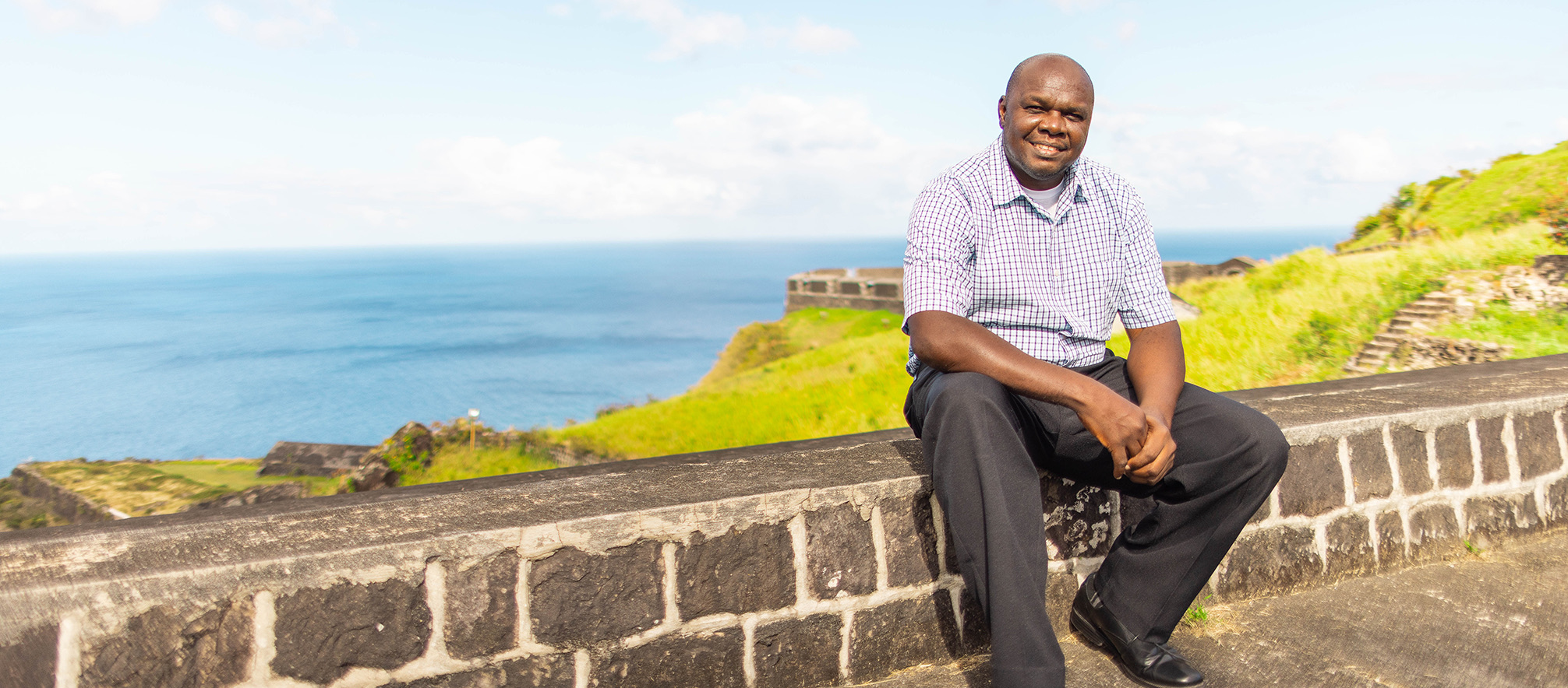 a man sitting on a stone wall overlooking a body of water