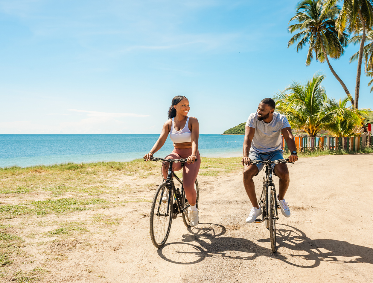 a man and woman riding bicycles on a dirt road by the ocean