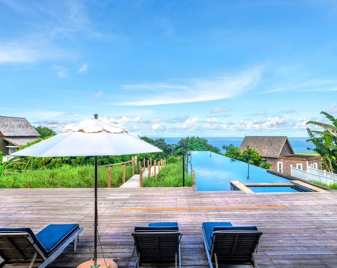 a deck with chairs and umbrellas and a pool with a body of water in the background