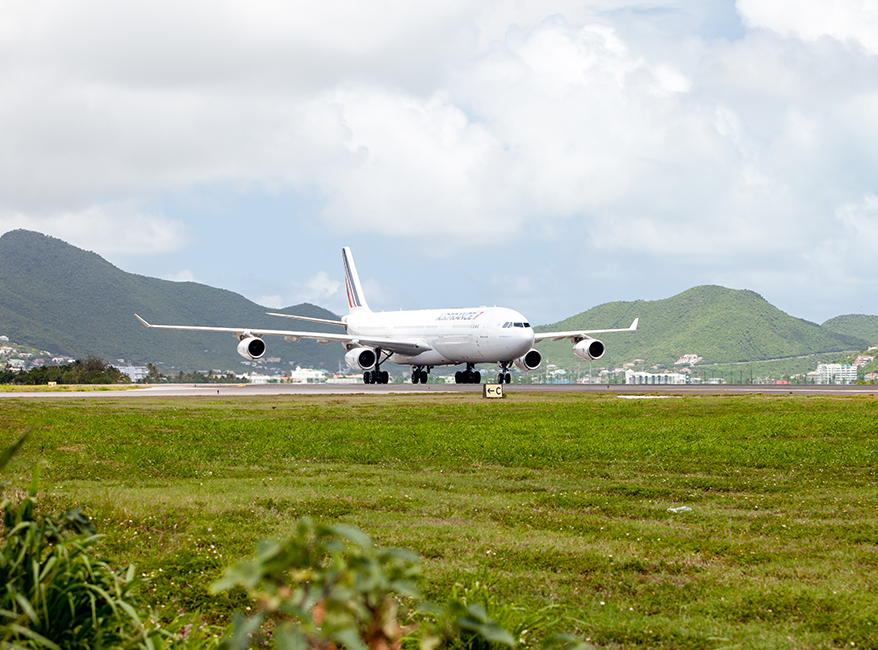 a large white airplane on a runway with green grass and mountains in the background