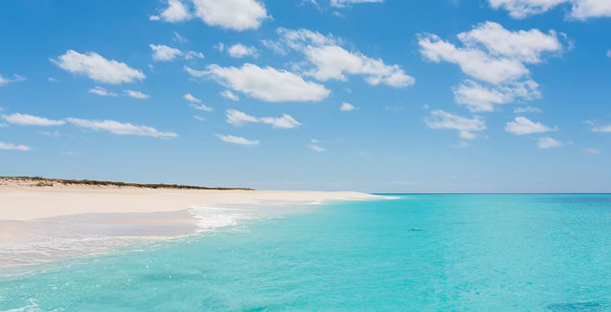 a beach with blue water and clouds