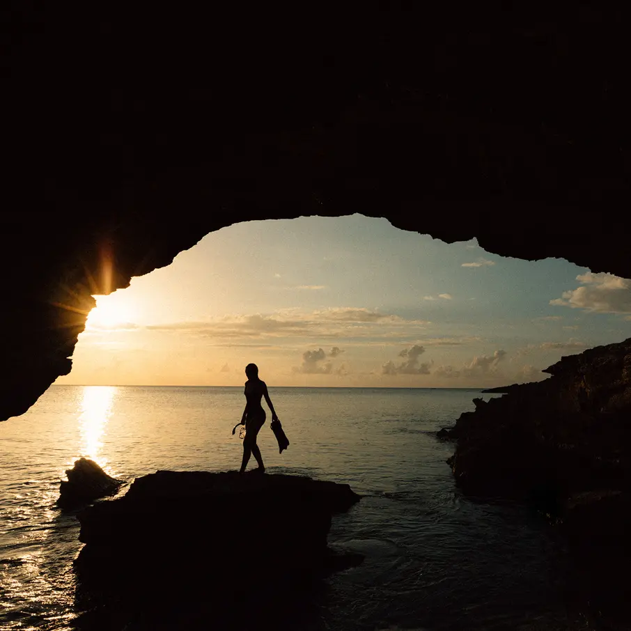 a silhouette of a woman walking on a rock in front of a body of water