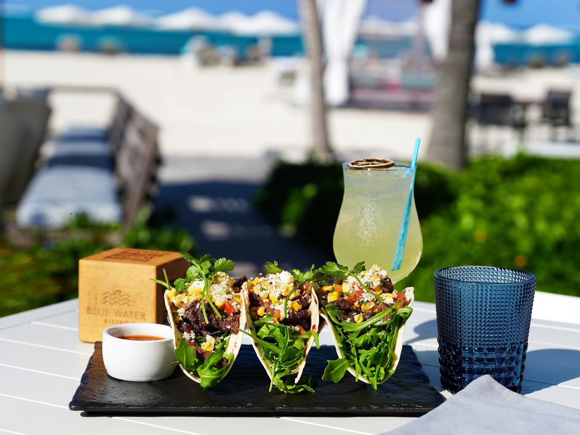 tacos on a table with a drink and a glass on the beach