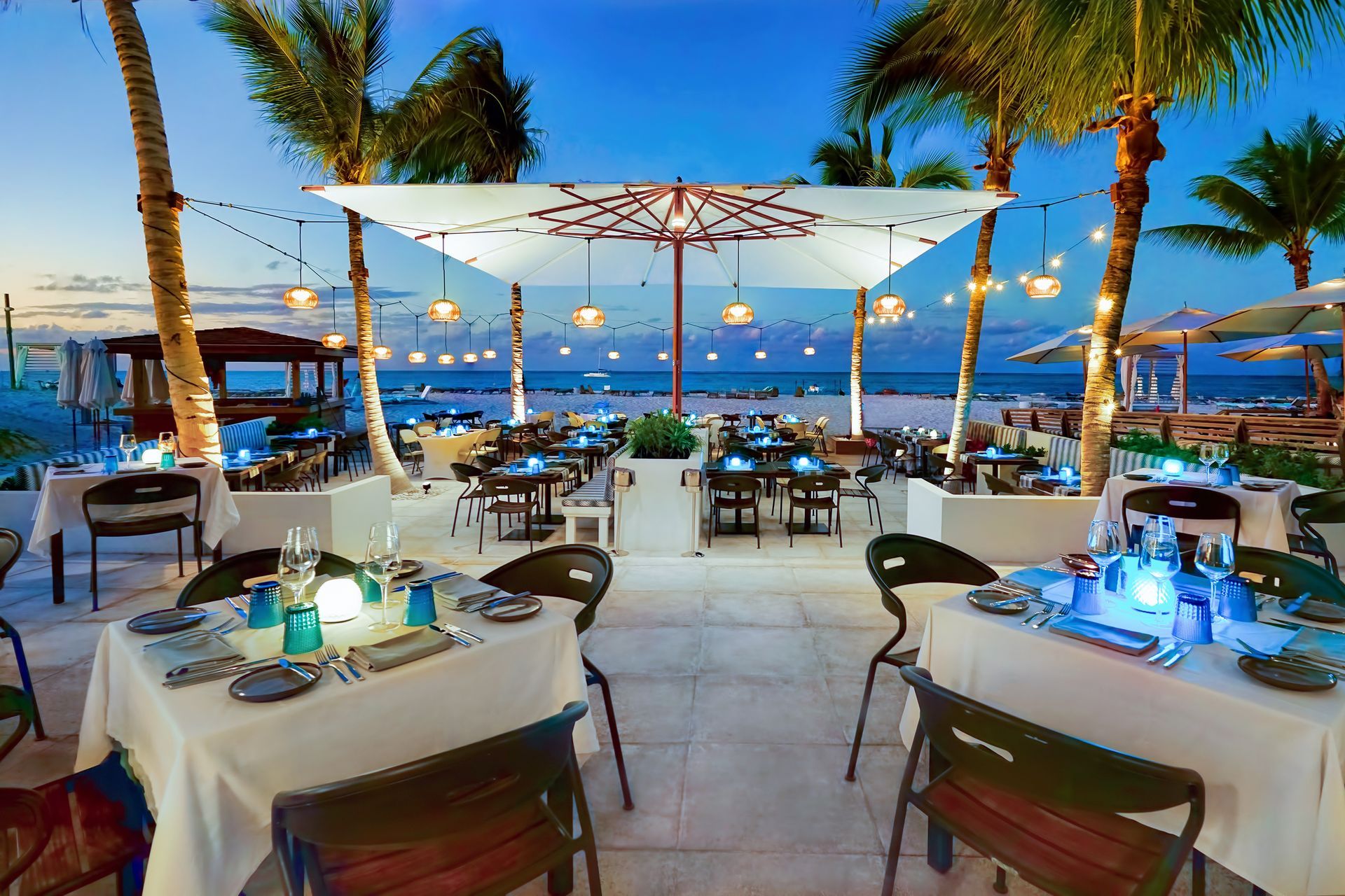 a restaurant with tables and umbrellas on the beach