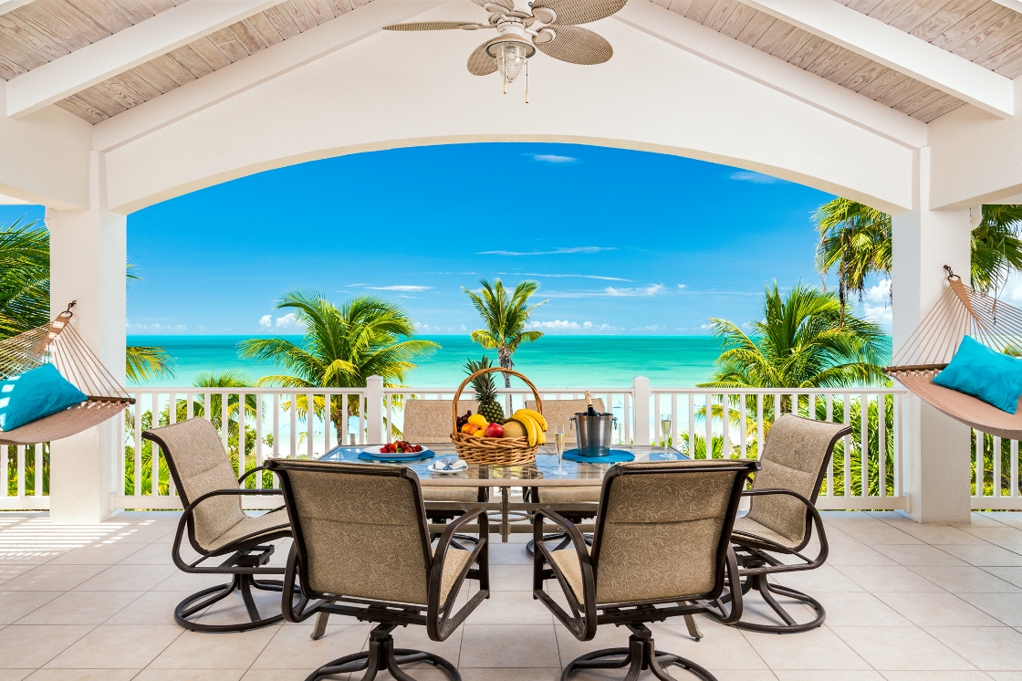 a table with fruit on it and chairs on a balcony overlooking the ocean
