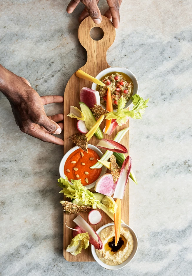 a hand holding a wooden board with food on it