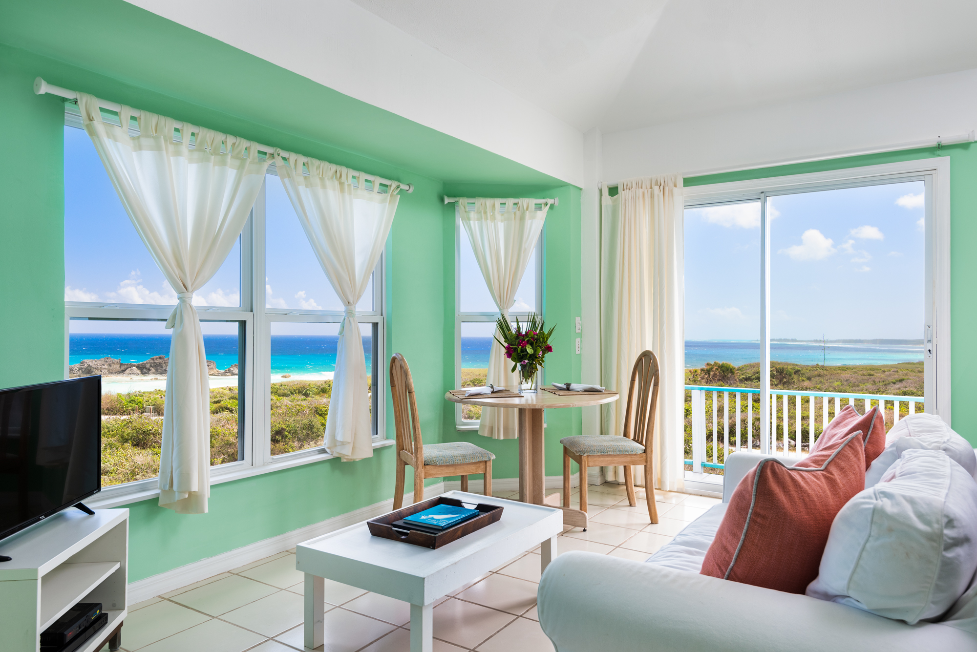 a living room with a table and chairs and a balcony overlooking the ocean