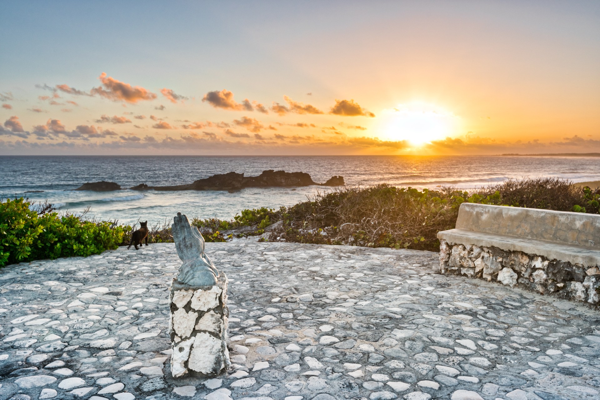 a stone bench and a statue on a stone walkway overlooking a body of water