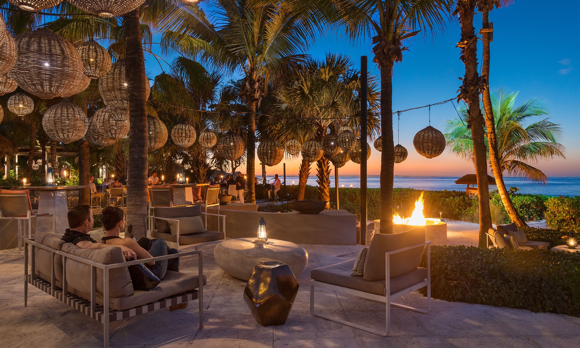 a fire pit with palm trees and a person sitting on a couch