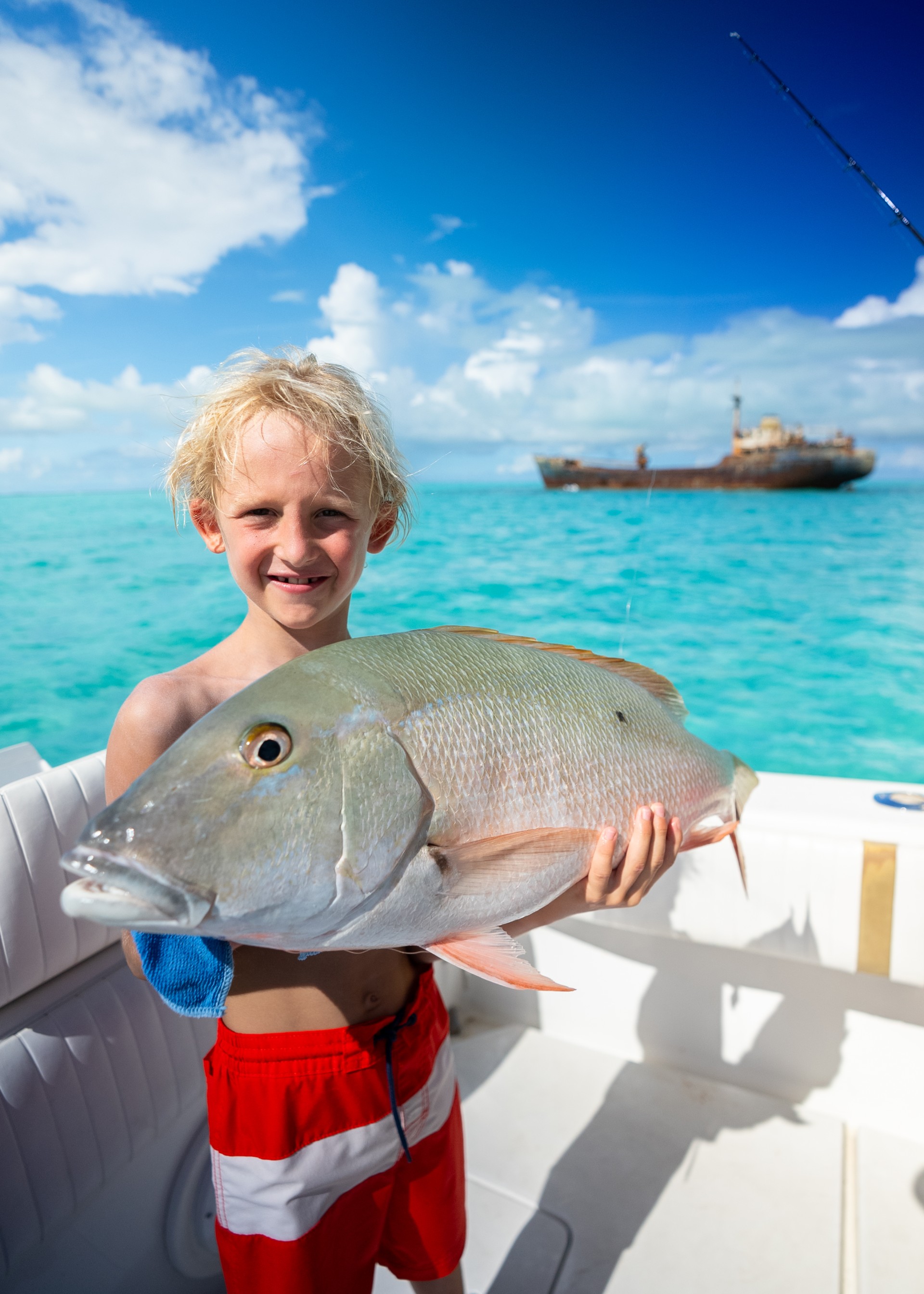 a boy holding a fish in front of a boat