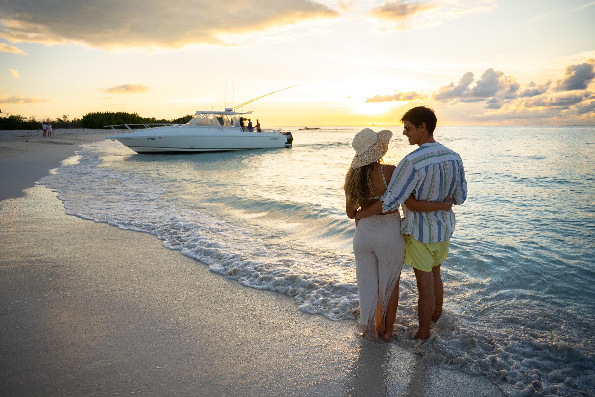 a man and woman standing on a beach with a boat in the background