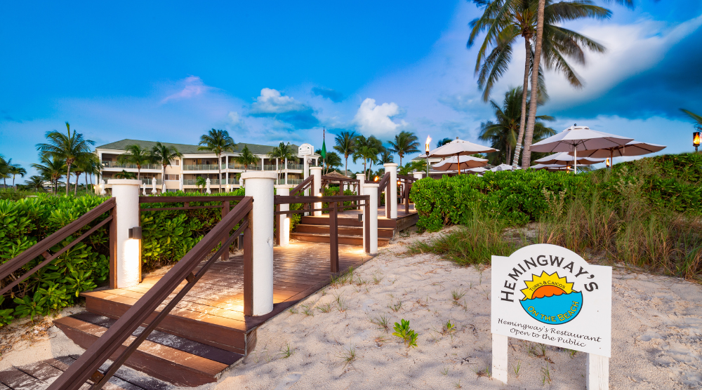 a walkway to a beach with palm trees and a building