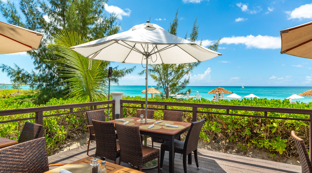 a table and chairs on a deck with a beach view