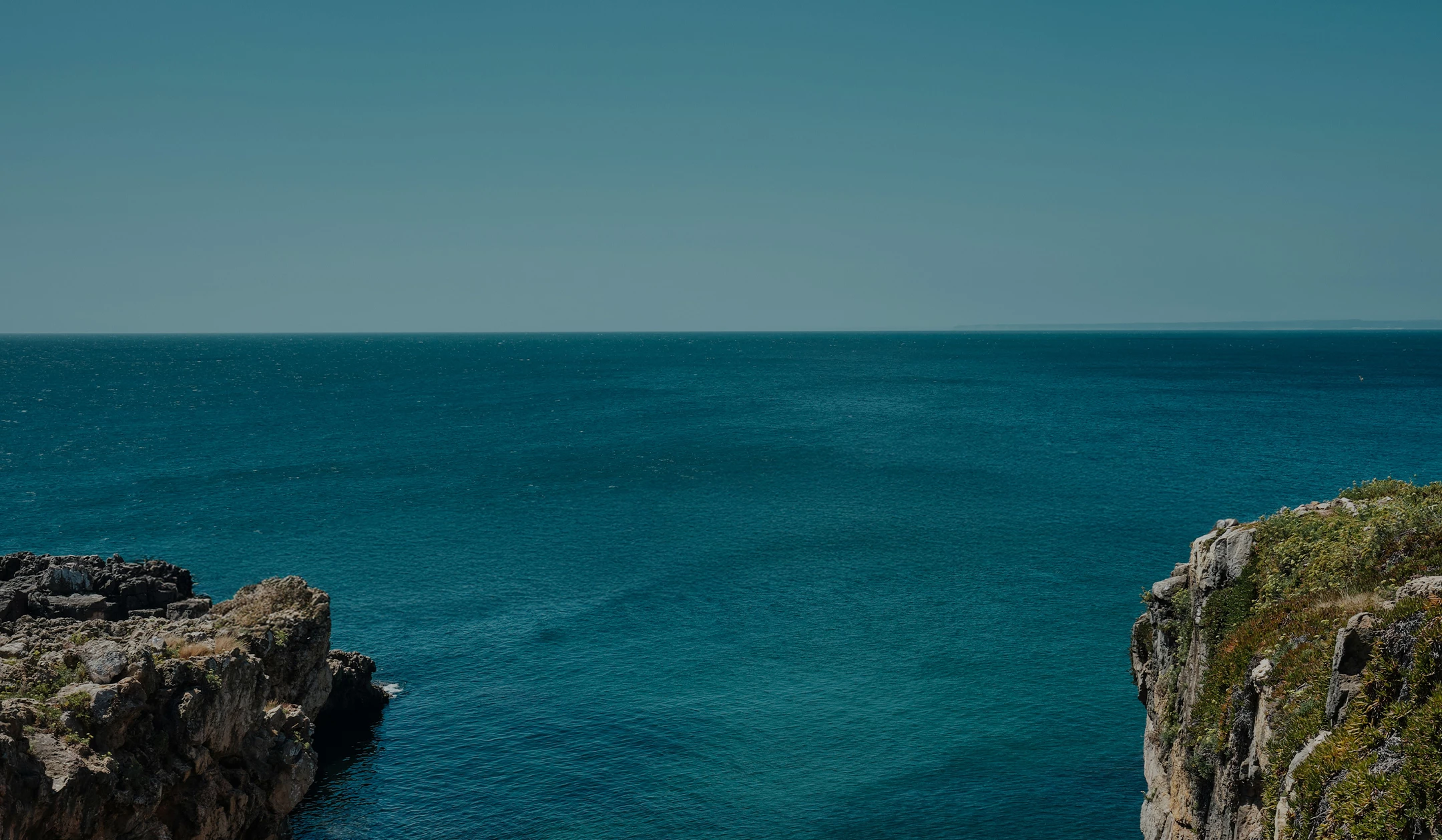 a large body of water with rocks and blue sky
