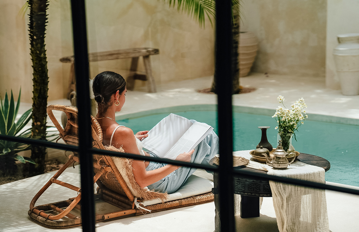 a woman sitting in a chair by a pool reading a book