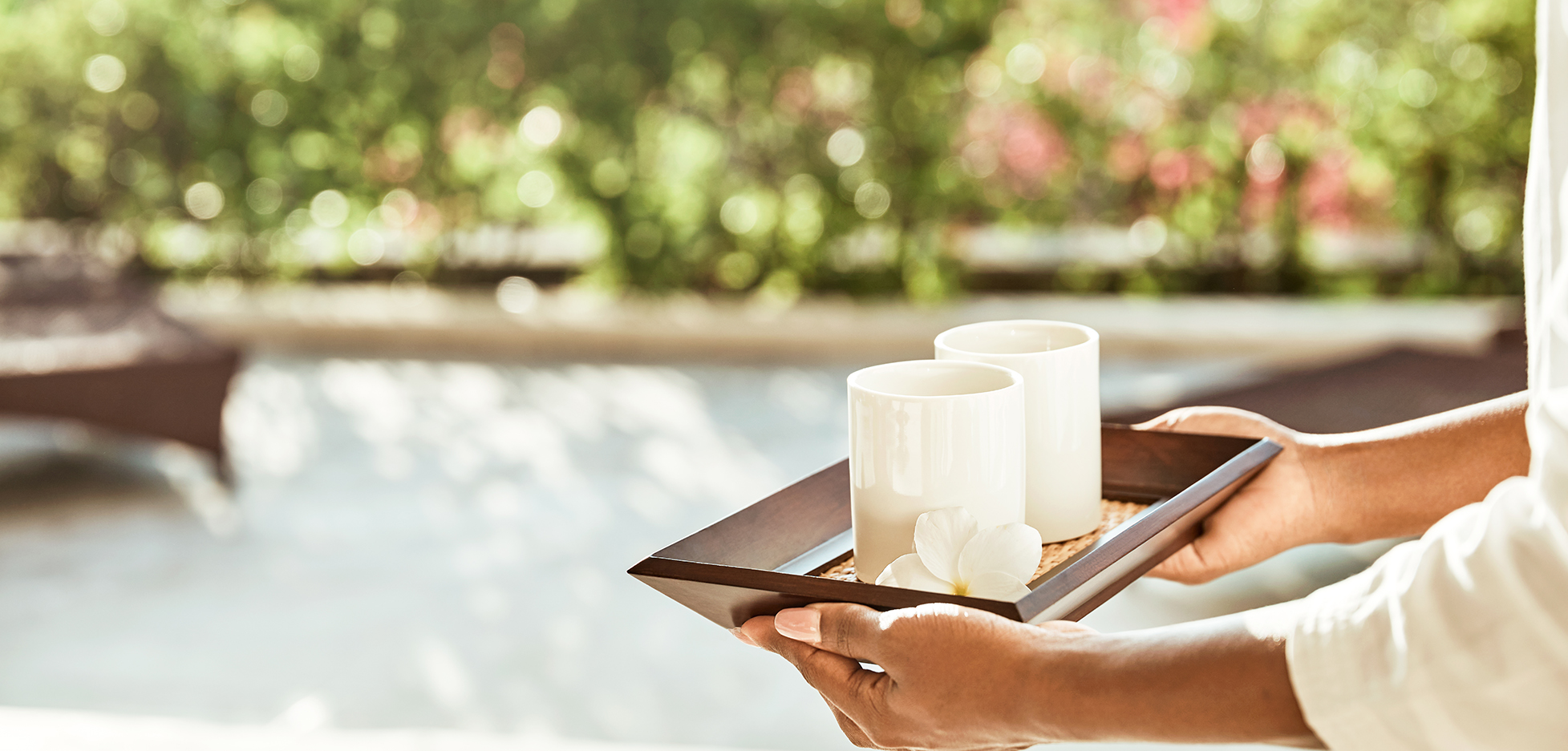 a person holding a tray with two white cups and a flower