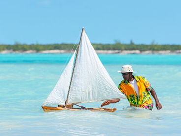 a man in a yellow shirt and hat with a sailboat in the water