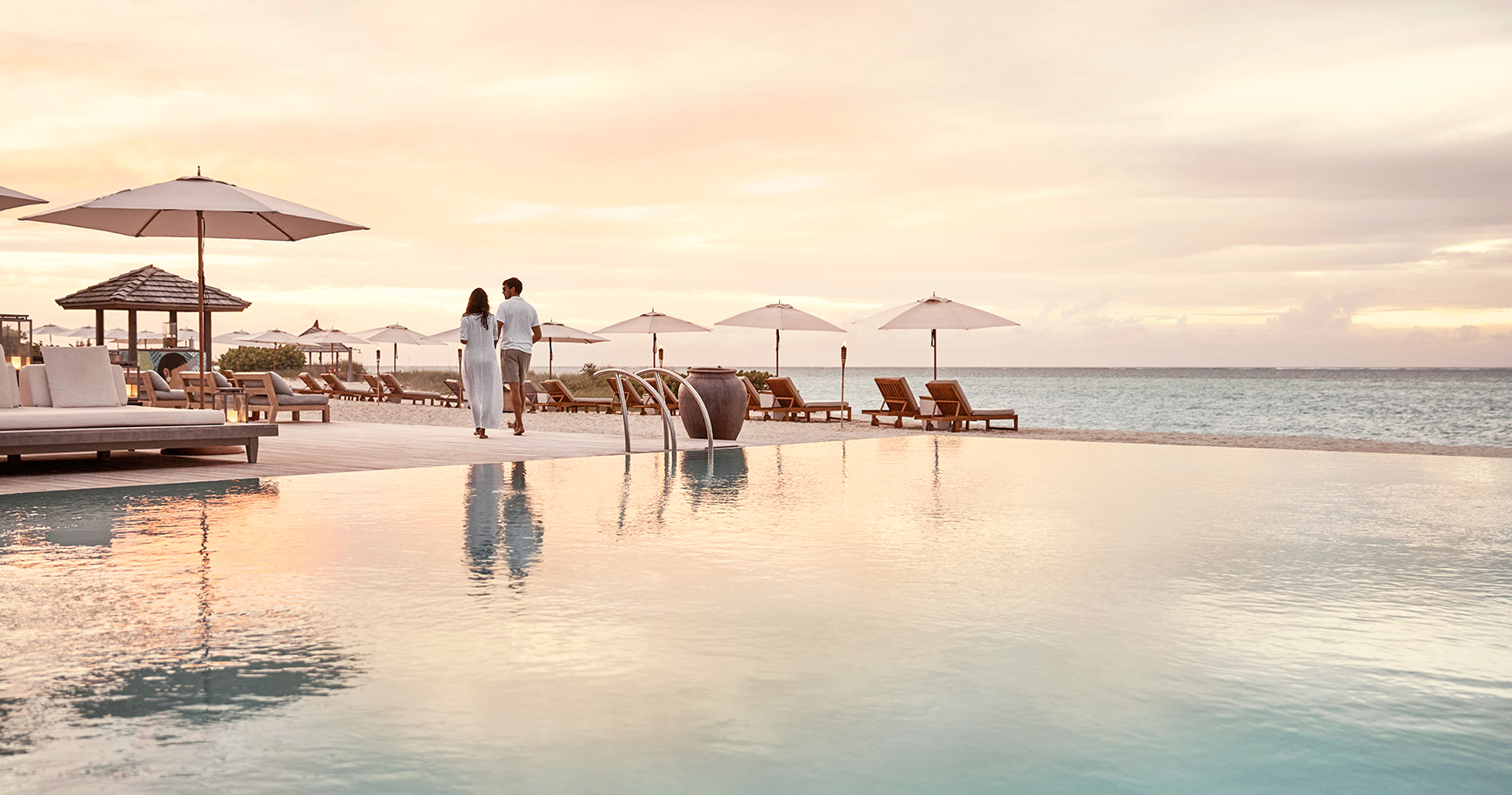 a man and woman walking by a pool with umbrellas and chairs