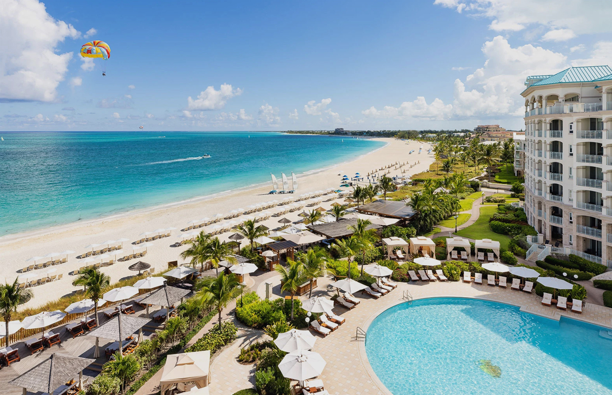 a swimming pool and beach with umbrellas and chairs