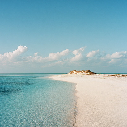 a sandy beach with blue water and clouds in the sky