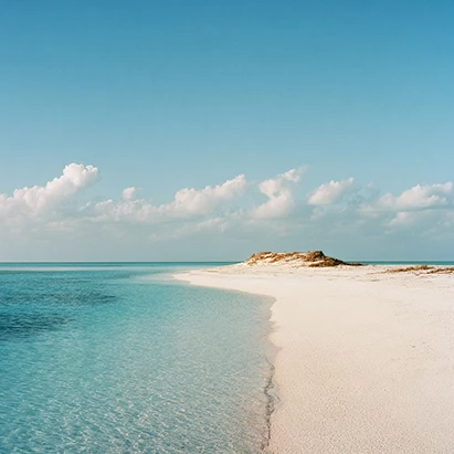 a sandy beach with blue water and clouds in the sky