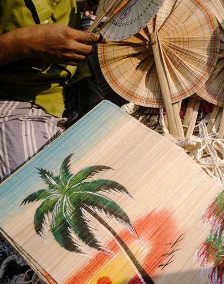 a person sitting on the ground with fan and palm trees