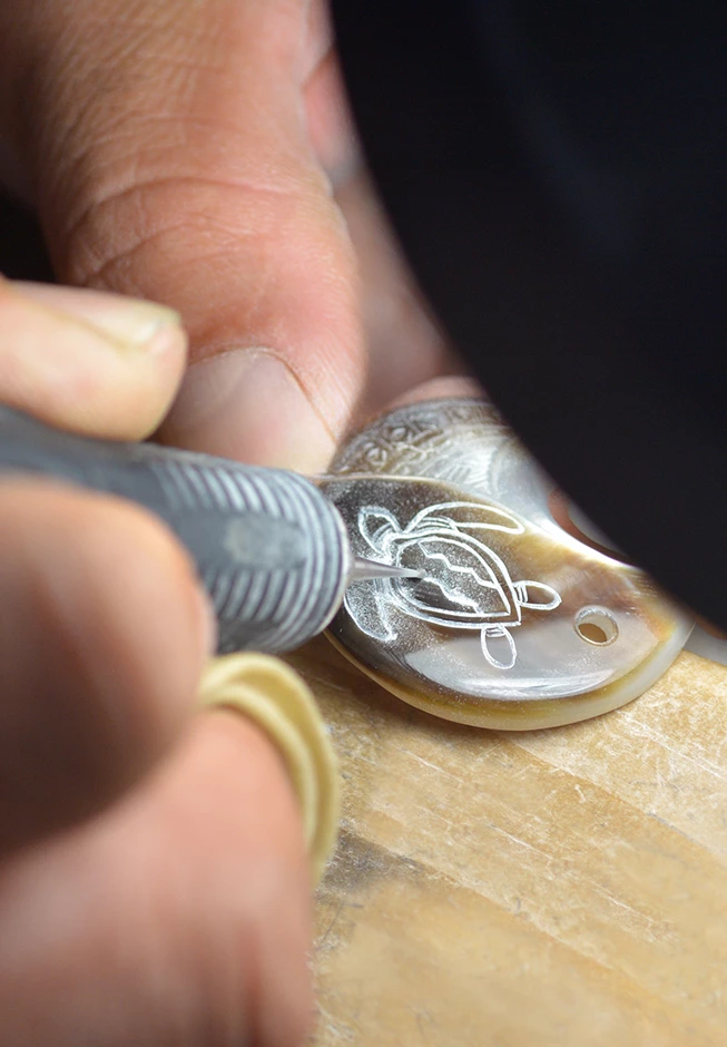 a person carving a turtle on a piece of shell