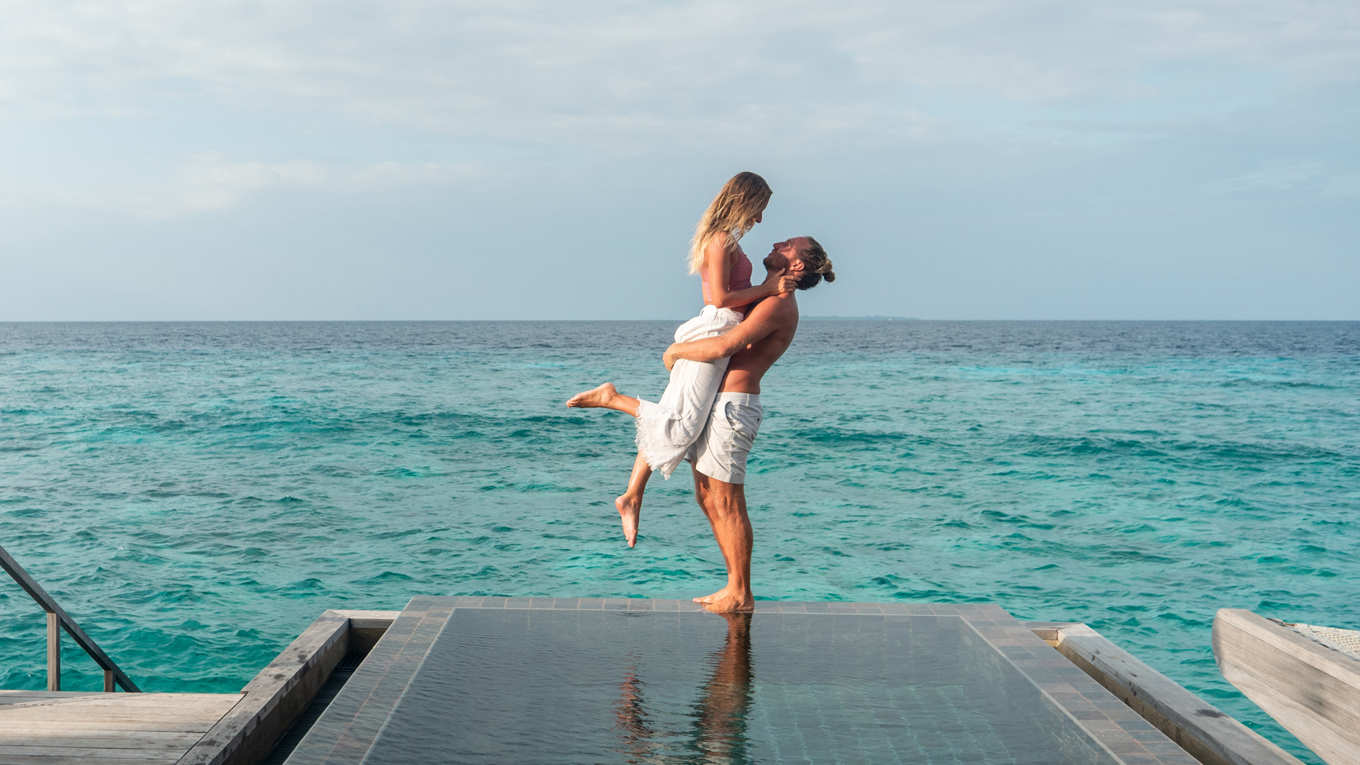 a man holding a woman on a ledge by the water
