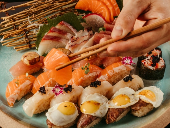 a hand holding chopsticks over a plate of sushi
