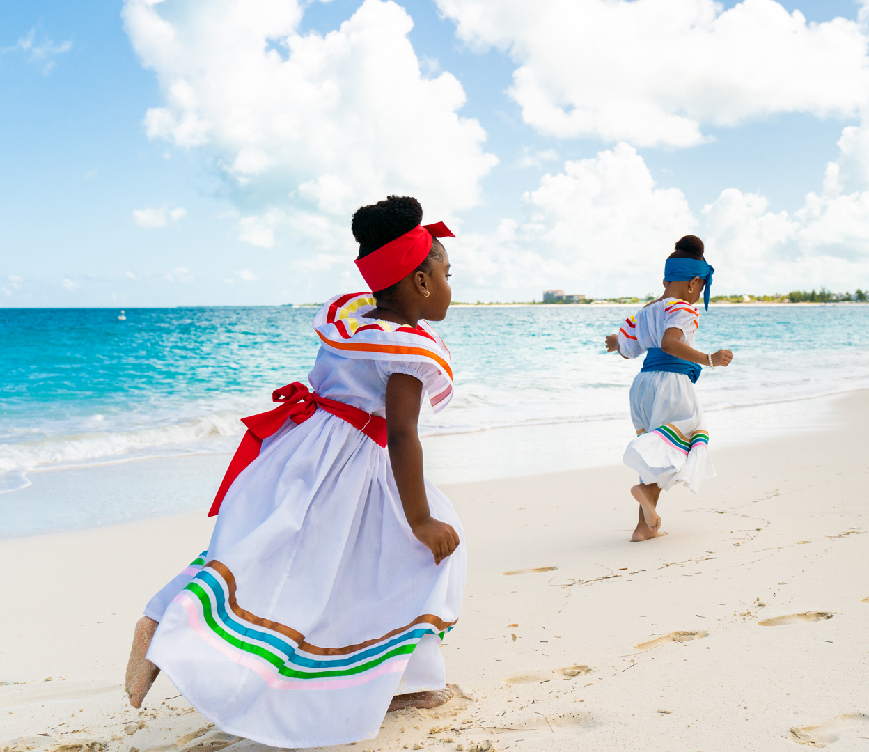 two girls in dresses running on a beach